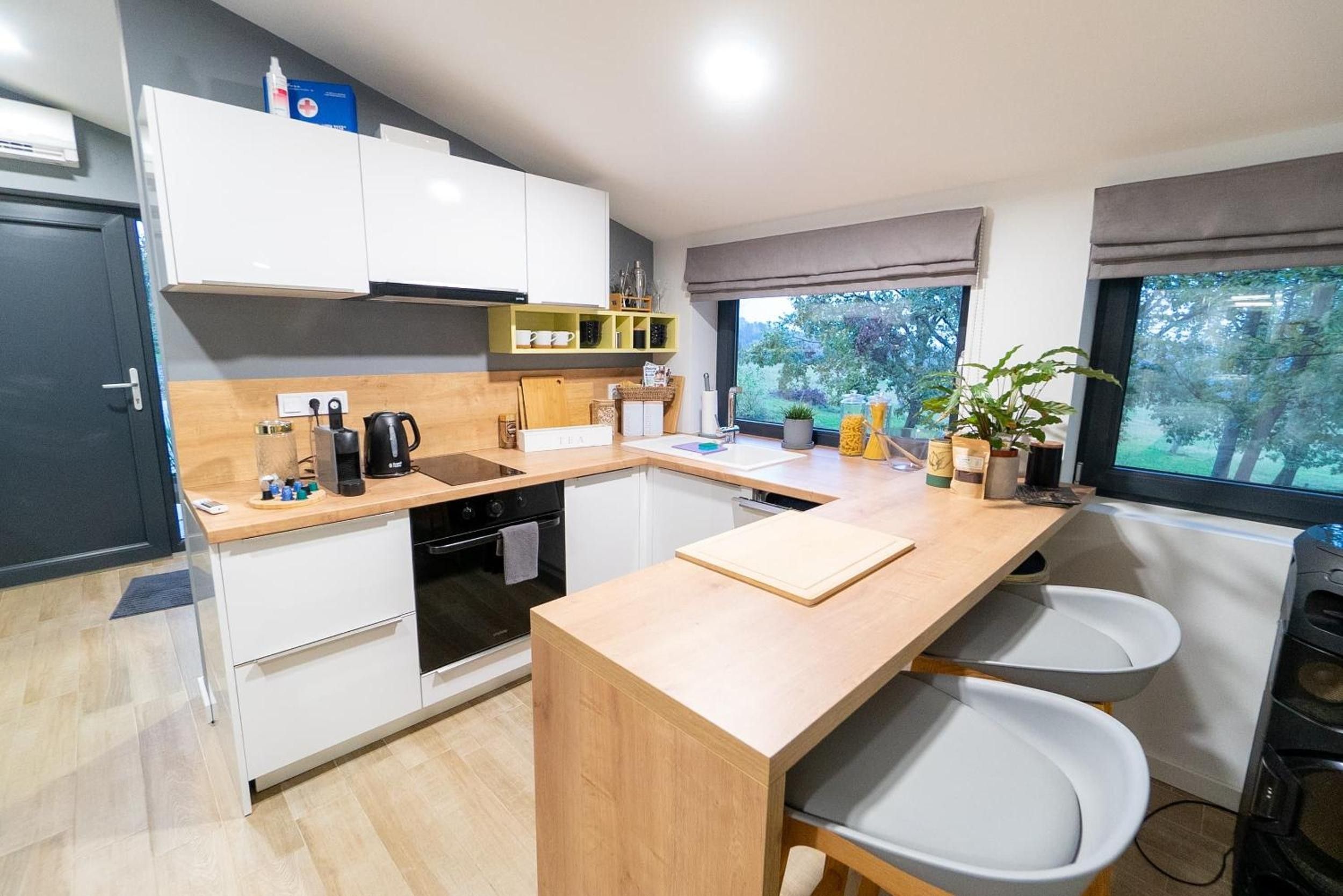 Una cocina moderna con armarios blancos, encimera de madera, horno integrado y ventana con vistas a árboles.