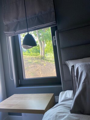 A room with a bed, a window with a view of trees, and a hanging lamp.