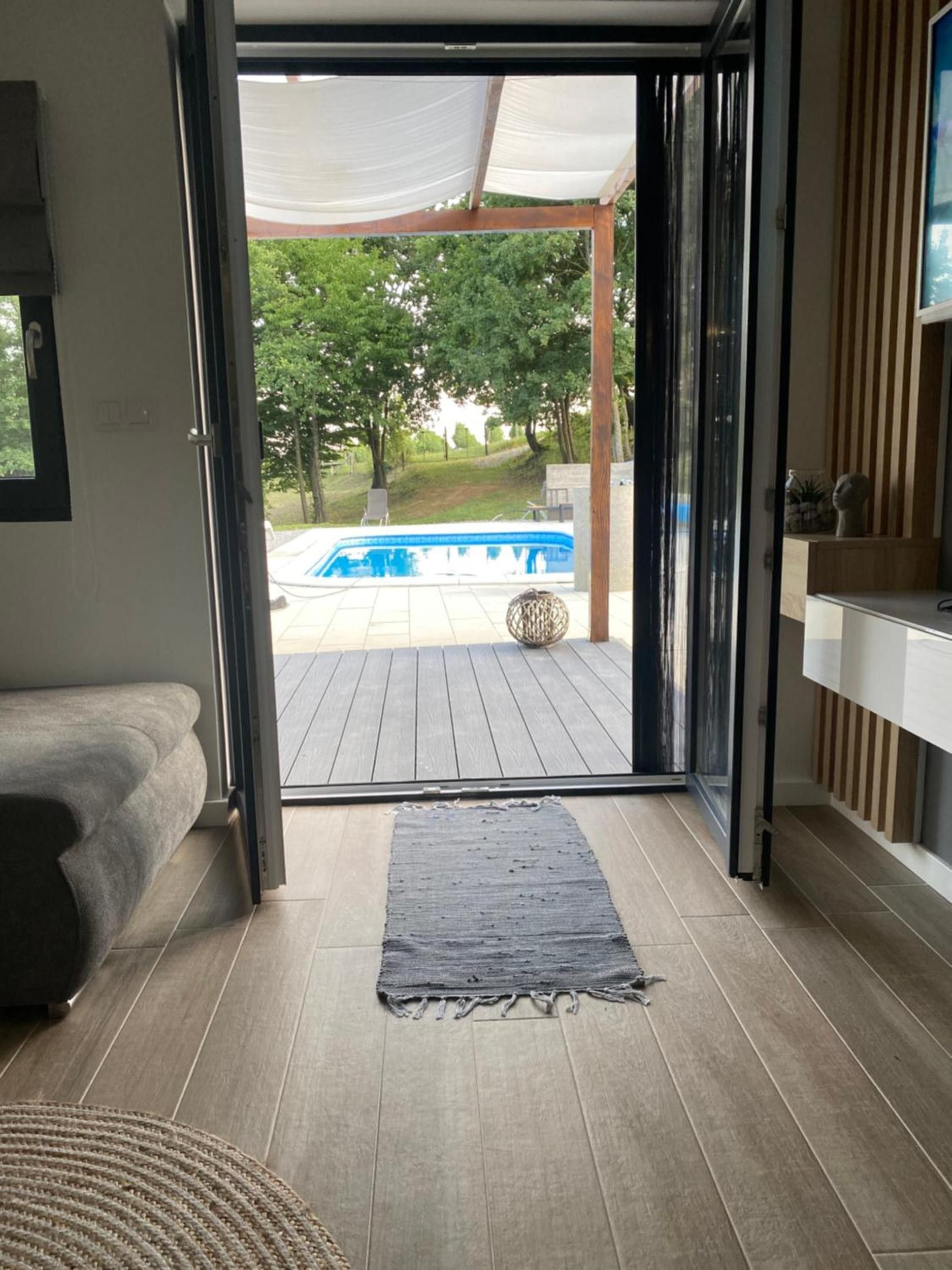 Eine geöffnete Tür führt auf eine Terrasse mit Pool, einer Couch und einem Teppich in einem Zimmer.