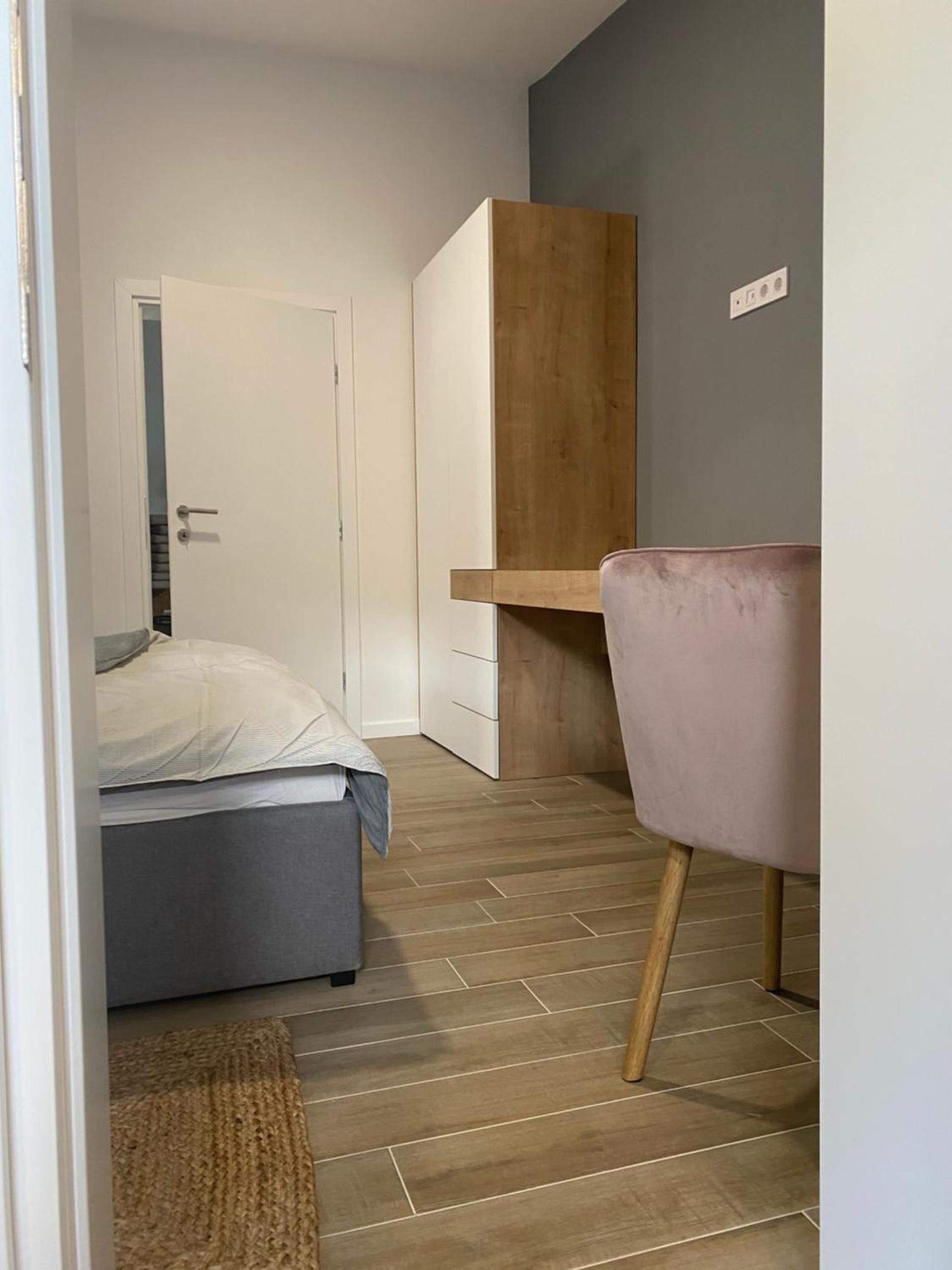 Un dormitorio con cama, escritorio y silla. Hay una puerta que da a otra habitación.