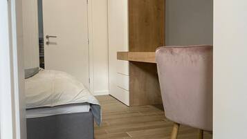 Un dormitorio con cama, escritorio y silla. Hay una puerta que da a otra habitación.