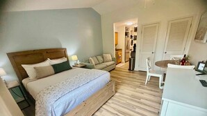 Un dormitorio con cama, mesitas de noche, un sofá, una mesa de comedor con sillas y una kitchenette.