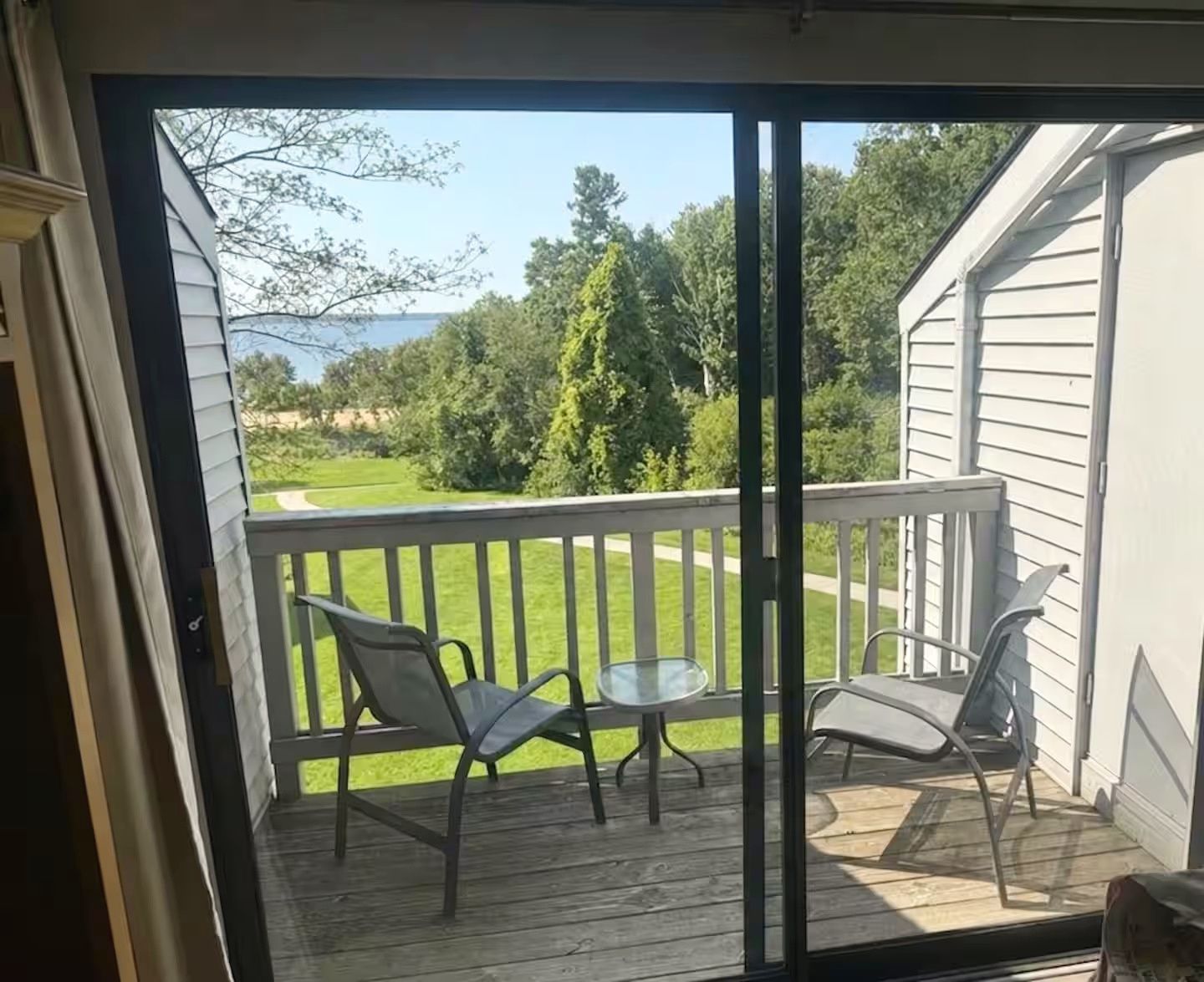 Een balkon met uitzicht op een gazon en bomen, twee stoelen en een klein tafeltje.