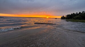 Una playa con olas, un atardecer y una costa lejana.