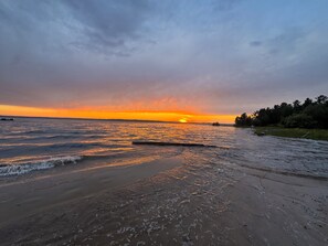 Een strand met golven, een zonsondergang en een verre kustlijn.