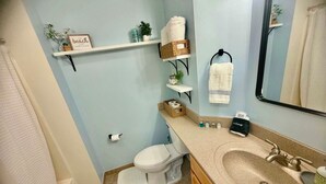 Un baño con inodoro, lavabo y repisas con toallas y artículos de aseo.