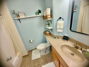 Een badkamer met toilet, wastafel en planken met handdoeken en toiletartikelen.