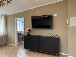 Ein modernes Wohnzimmer mit einem flachbildfernseher an der Wand, einer dunklen Unterhaltungseinheit darunter und einem Holzboden.