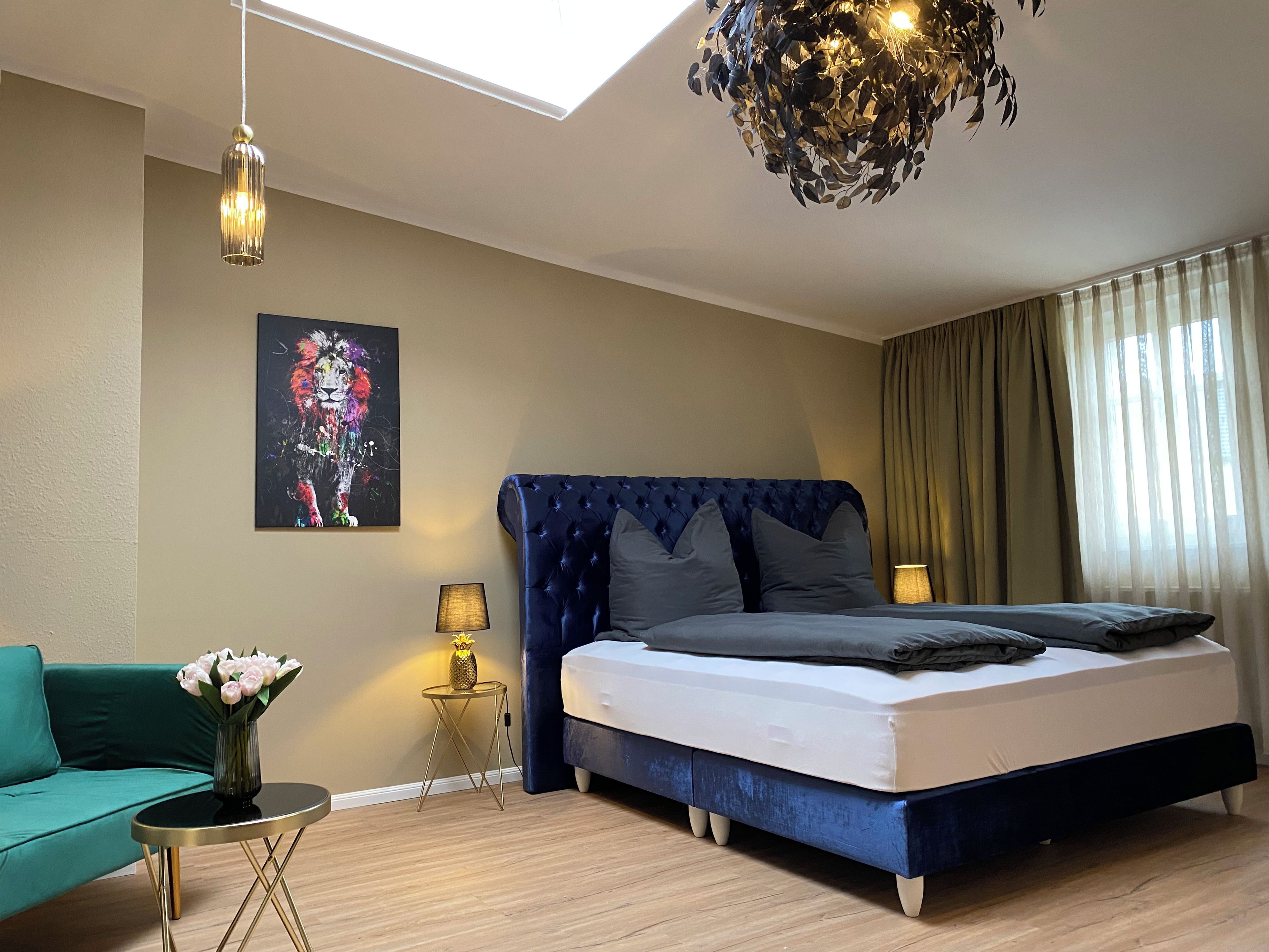 Ein Schlafzimmer mit einem Bett, einem Sofa, einem kleinen Tisch mit Lampe, einem Bild an der Wand und einer Deckenleuchte.