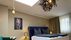 A bedroom with a bed, a sofa, a small table with a lamp, a painting on the wall, and a ceiling light fixture. - Zur Post 1 (Bautzen)