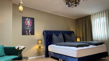 Ein Schlafzimmer mit einem Bett, einem Sofa, einem kleinen Tisch mit Lampe, einem Bild an der Wand und einer Deckenleuchte.