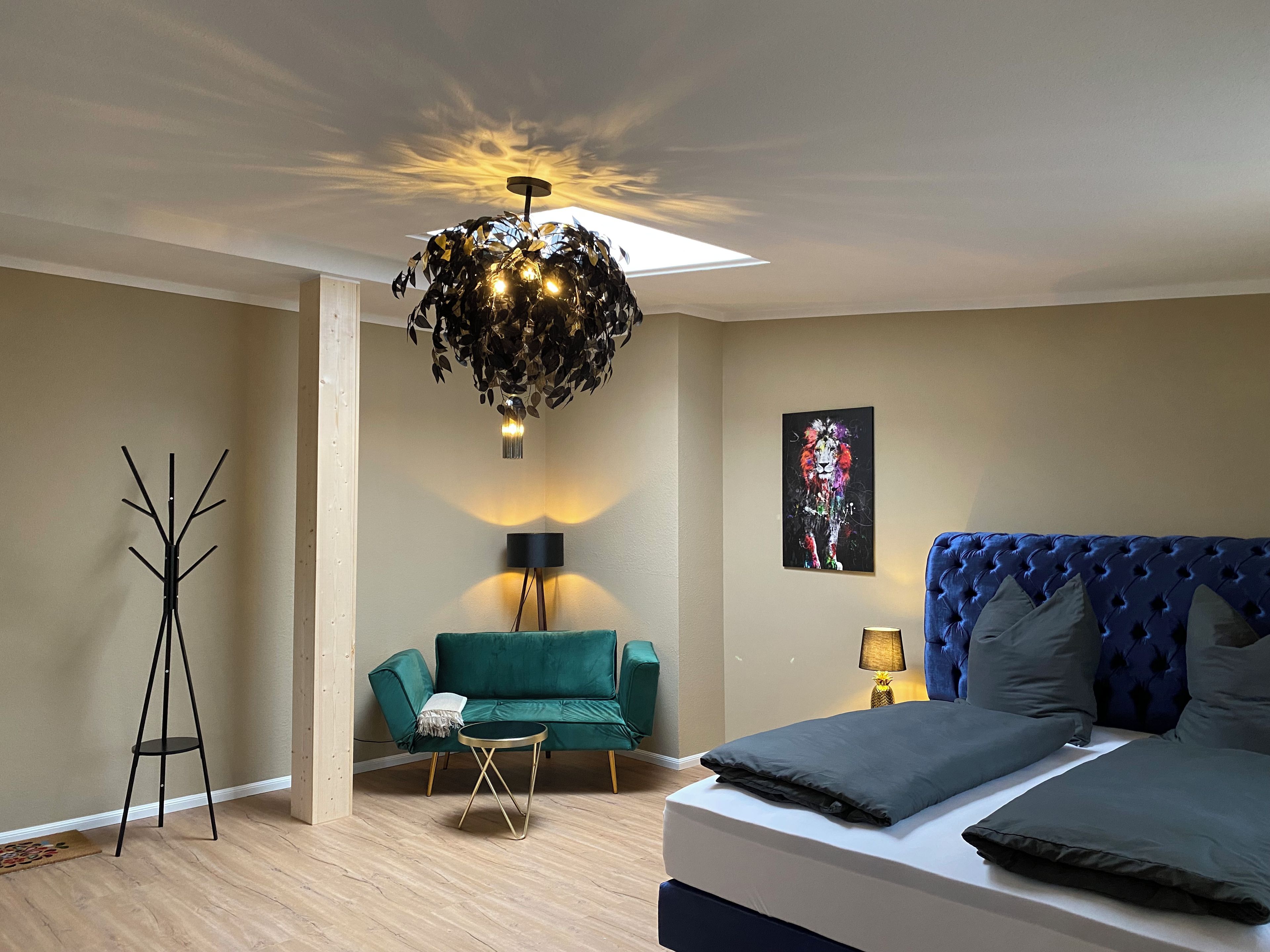 Ein Schlafzimmer mit einem Bett, einem grünen Sofa, einer Stehlampe und einer Deckenleuchte.