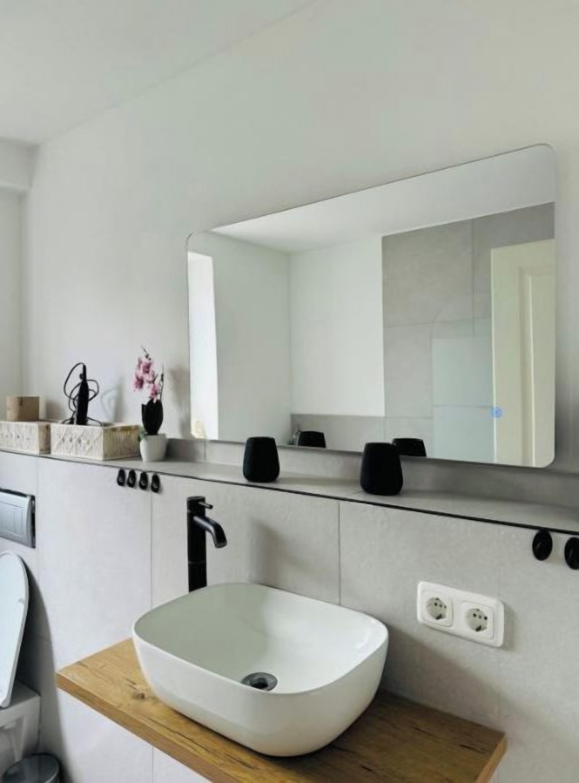 Ein modernes Badezimmer mit einem weißen Waschbecken, einem großen Spiegel und einer Holzauslage.