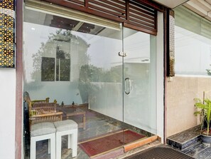 Ein Glastür-Eingang mit Holzlamellen-Design, eine kleine Sitzgelegenheit mit einer Bank und zwei Hockstühlen sowie ein Blumentopf auf der rechten Seite.