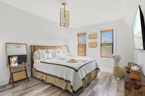 A bedroom with a bed, bedside tables, a mirror, a hanging light fixture, and a television. - 3 beds/2.5 bath, A-Frame Palm Tree & Alpaca & Llama Farm (Palm Beach Gardens)