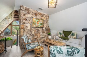 A living room with a stone wall, a sofa, a coffee table, and a chair with a globe lamp. - 3 beds/2.5 bath, A-Frame Palm Tree & Alpaca & Llama Farm (Palm Beach Gardens)