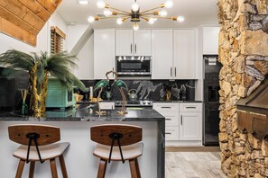 A modern kitchen with white cabinets, a central island with bar stools, a stone accent wall, and a ceiling light fixture. - 3 beds/2.5 bath, A-Frame Palm Tree & Alpaca & Llama Farm (Palm Beach Gardens)