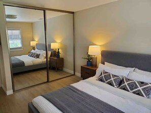 Un dormitorio con cama, mesitas de noche, lámparas, un espejo y una puerta corredera que da a otra habitación.