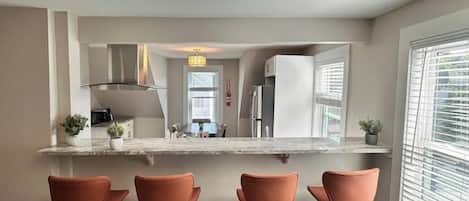 A modern kitchen with a bar area, wooden flooring, and a large window.