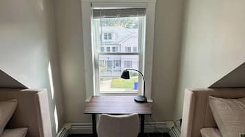 A bedroom with a desk and chair, a window with blinds, and a view of a house outside.