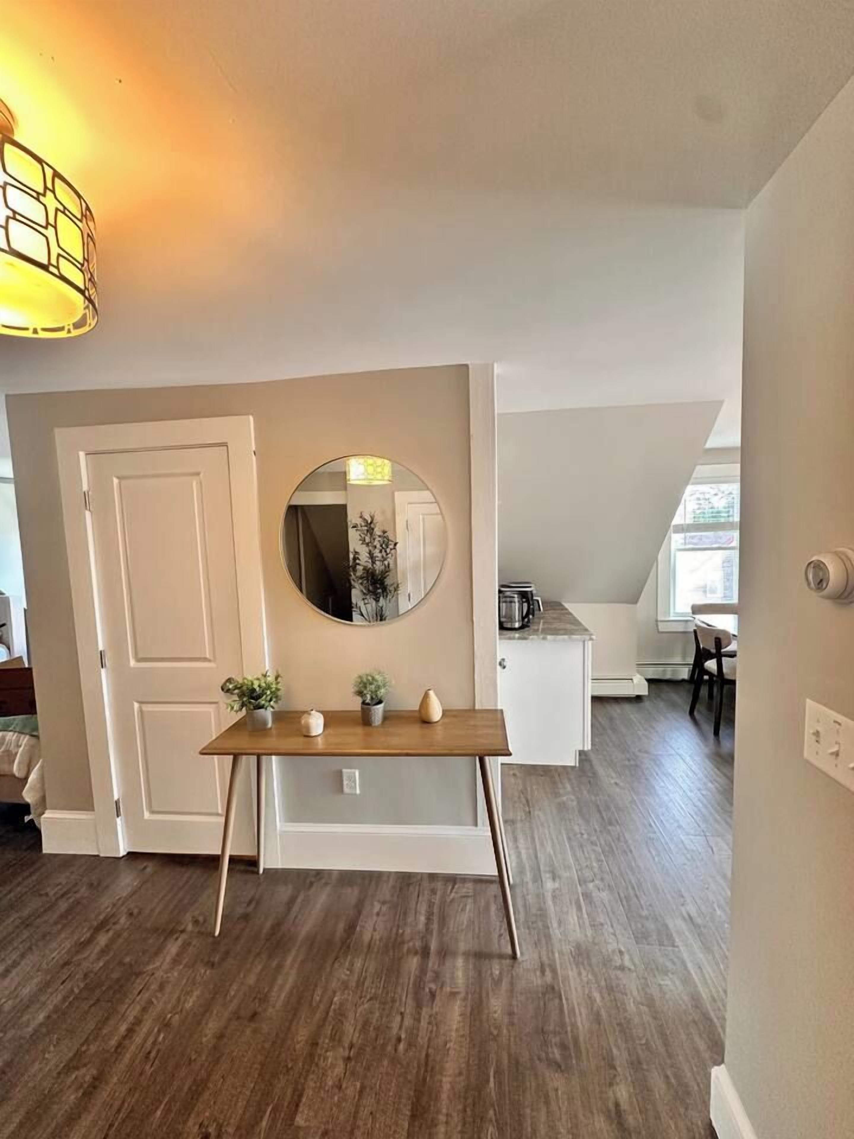 A room with a wooden table, a round mirror, and a door.