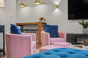 Een moderne woonkamer met twee roze fauteuils, een houten salontafel, een flatscreen televisie en een open haard.