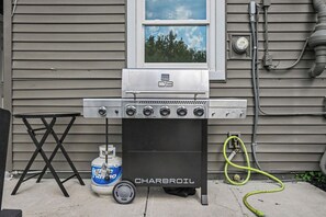 A Charbroil barbecue grill with a gas tank and propane canister, hoses, and a window above it.