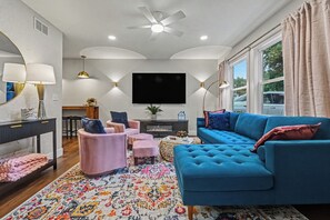 A modern living room with a blue sofa, pink armchairs, a TV, and a fireplace.