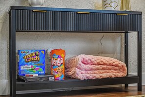 A shelf with a board game, a Jenga box, and a pink blanket.