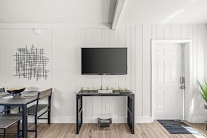 Una sala moderna con comedor, un televisor negro montado en la pared, un adorno en la pared y una puerta con una planta pequeña a su lado.