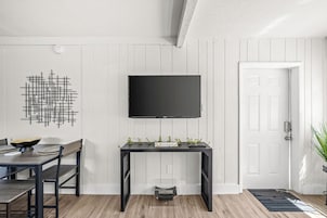 Una sala moderna con comedor, un televisor negro montado en la pared, un adorno en la pared y una puerta con una planta pequeña a su lado.