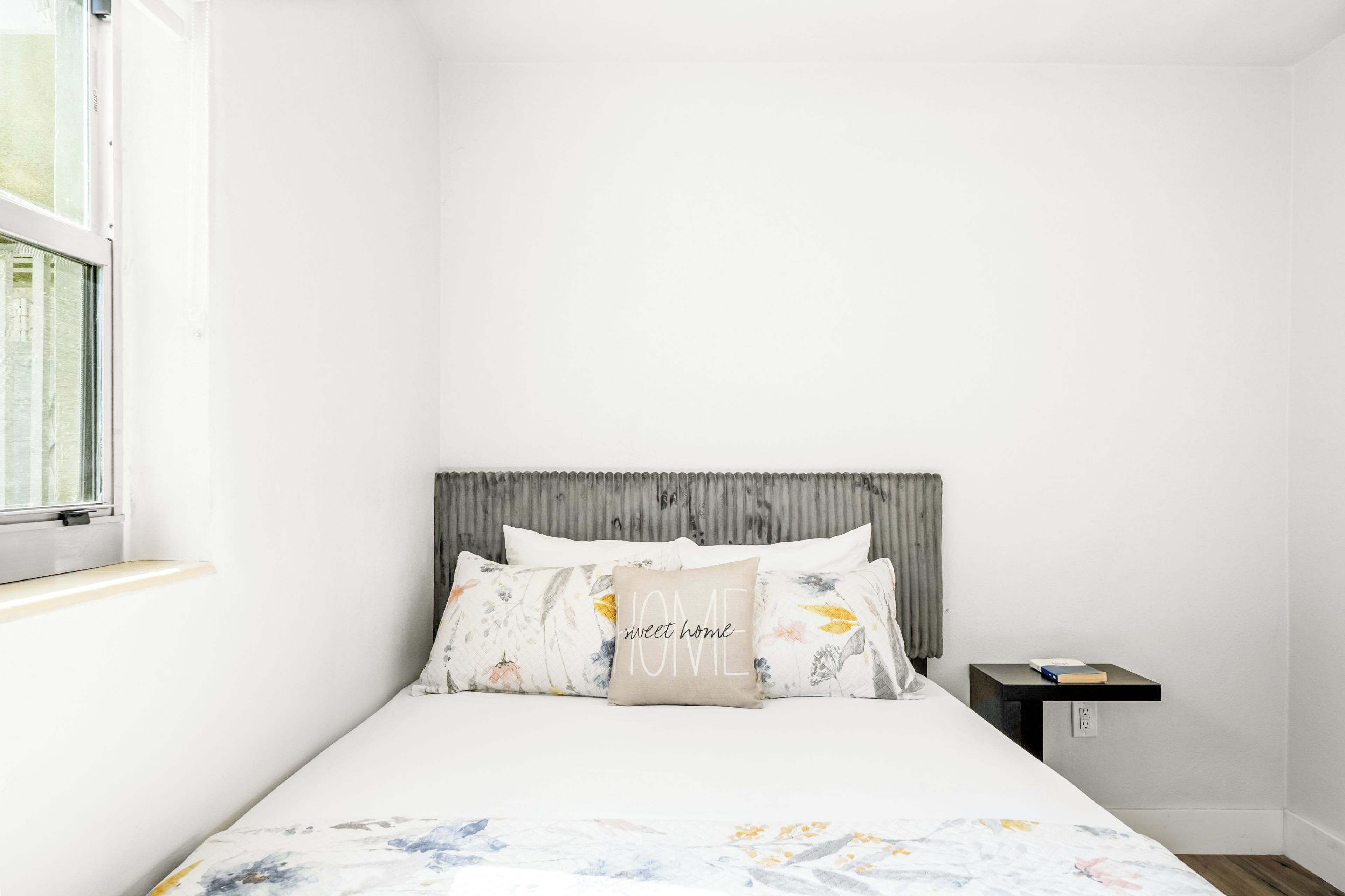 A bedroom with a bed, a nightstand, a window, and a headboard.
