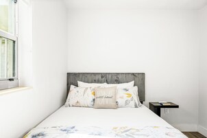 A bedroom with a bed, a nightstand, a window, and a headboard.