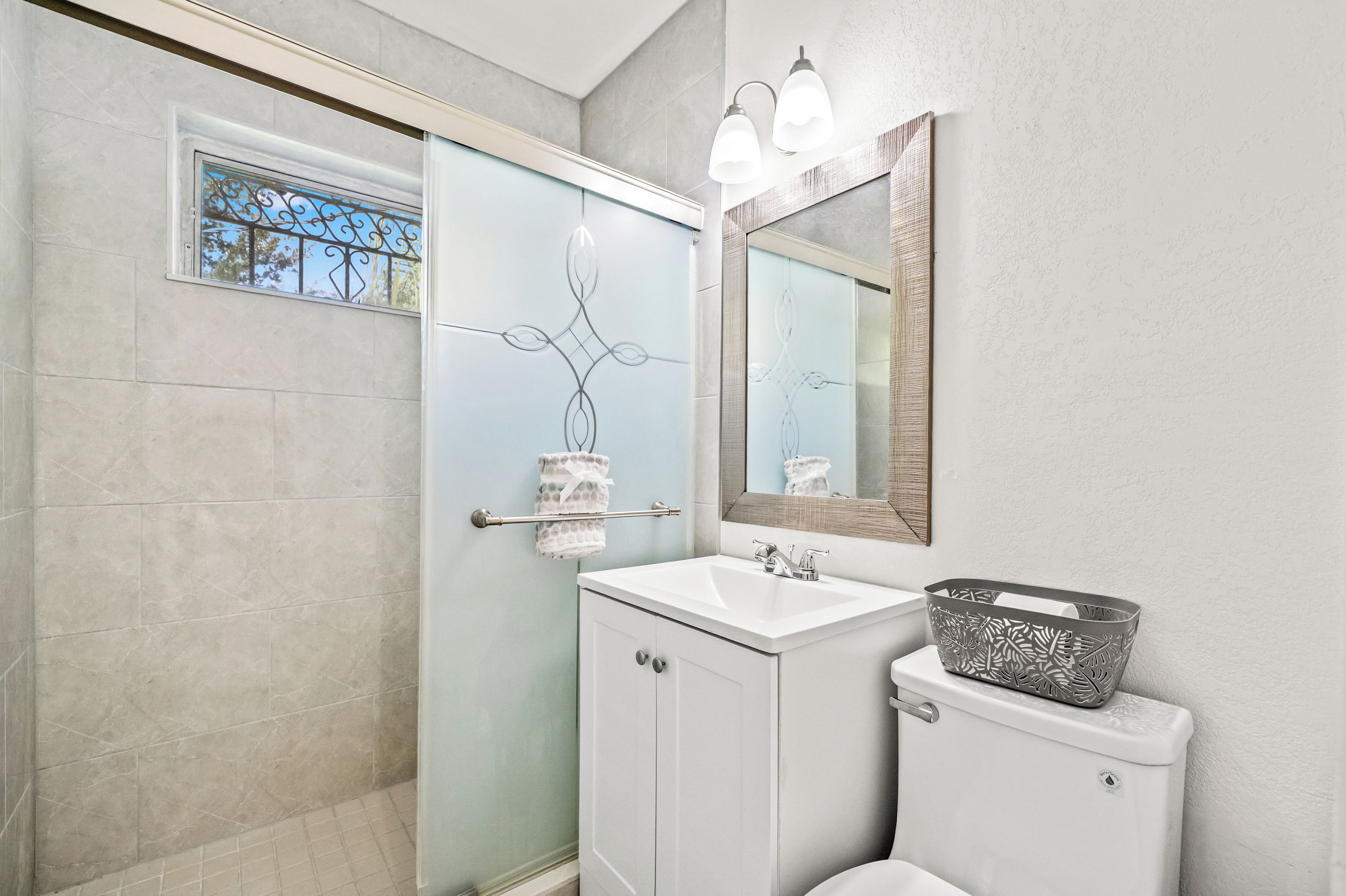 A bathroom with a glass shower door, a white sink, a toilet, and a mirror with lights.