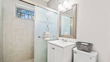 A bathroom with a glass shower door, a white sink, a toilet, and a mirror with lights.