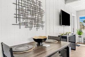 Un comedor con mesa de madera, sillas negras, un centro de mesa con un cuenco negro y un televisor montado en la pared.