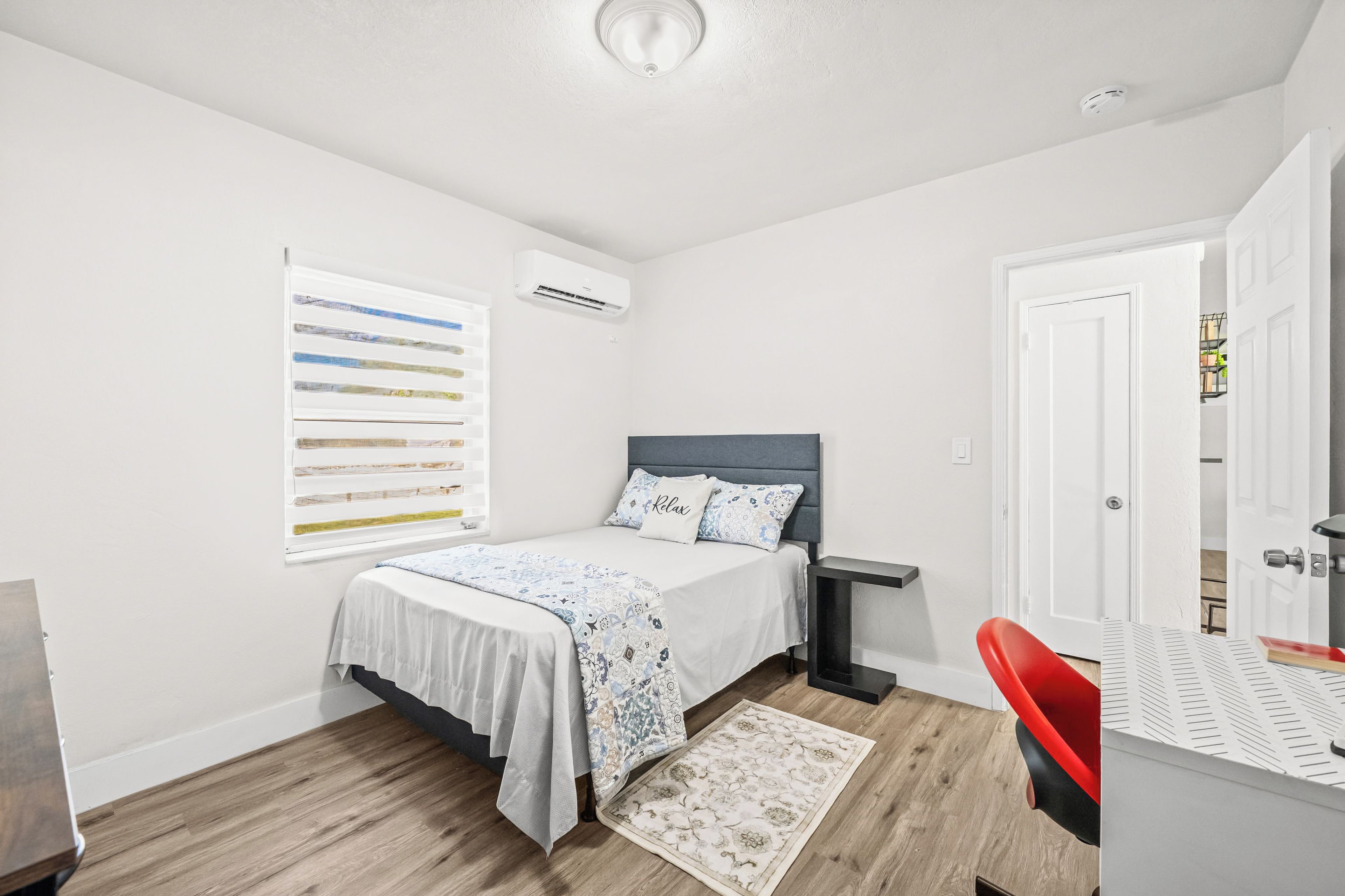 A bedroom with a bed, bedside table, and a window with blinds.