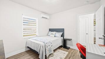 A bedroom with a bed, bedside table, and a window with blinds.