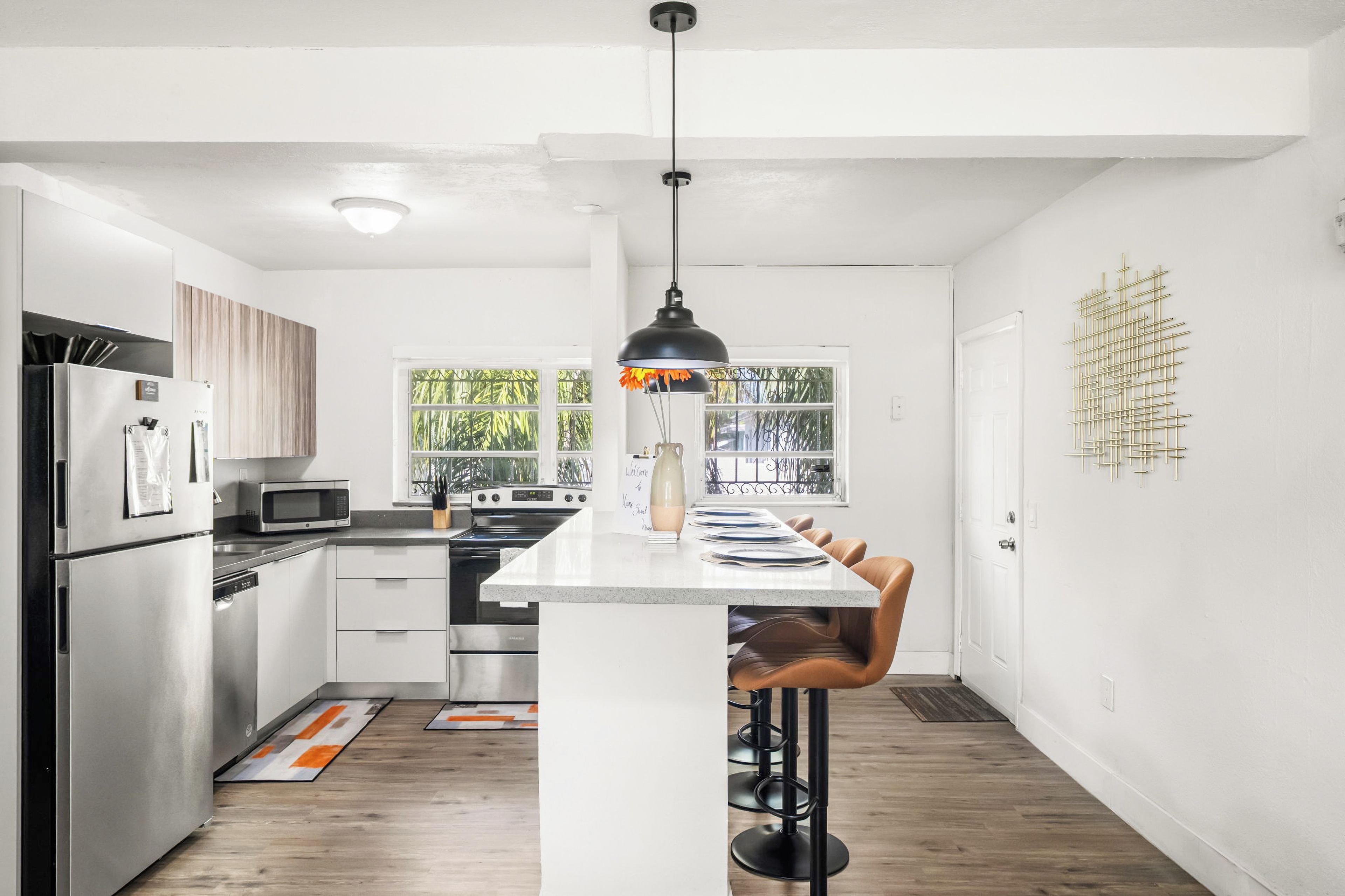Una cocina moderna con electrodomésticos de acero inoxidable, una isla central con taburetes y vistas a zonas verdes por las ventanas.