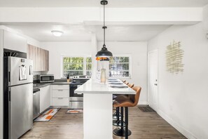 Una cocina moderna con electrodomésticos de acero inoxidable, una isla central con taburetes y vistas a zonas verdes por las ventanas.