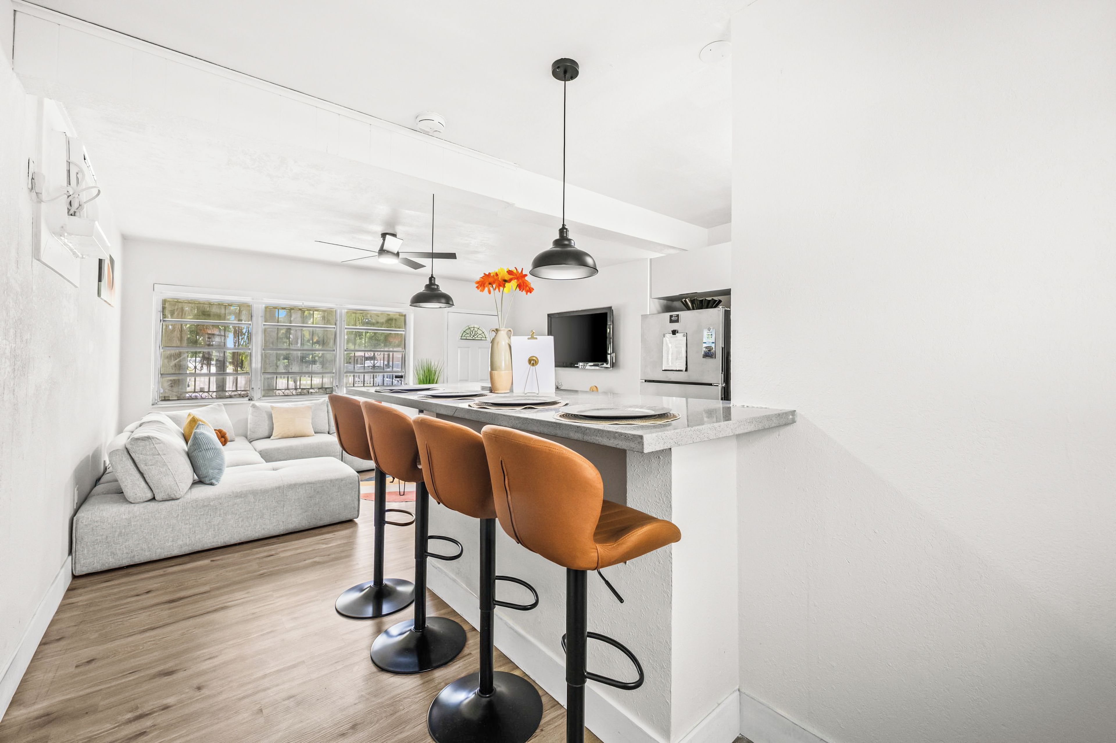 A modern kitchen with a bar area, a grey sofa, and a dining table.
