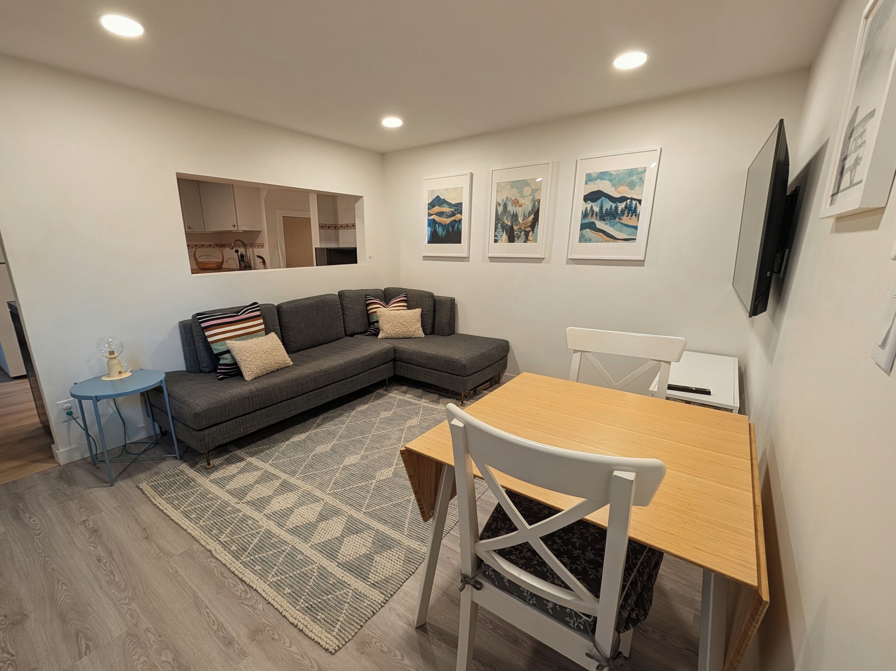 A modern living room with a sectional sofa, a dining table with chairs, a patterned rug, and framed artwork on the wall.
