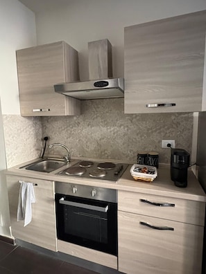 A modern kitchen with a stainless steel sink, a stove, and a black oven. There are cabinets above the counter and a range hood above the stove. - Rubino | Urban Suite (Valenza)
