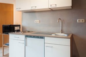 Una cocina moderna con armarios blancos, un lavamanos de acero inoxidable y un microondas.