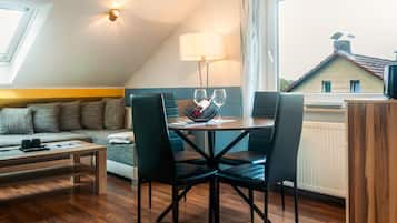 Ein gemütliches, helles Wohnzimmer mit Essbereich, einer Couch und Blick auf ein Haus durch ein Fenster.