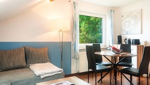 A cozy room with a sofa, a dining table with chairs, a lamp, and a view of greenery outside.