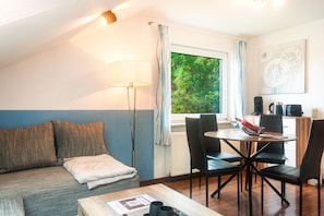 A cozy room with a sofa, a dining table with chairs, a lamp, and a view of greenery outside.
