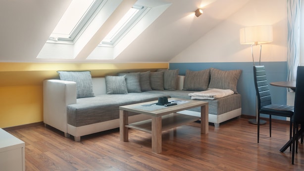 A modern loft-style room with a sloped ceiling, a sofa set, a coffee table, a lamp, and a view through skylights.