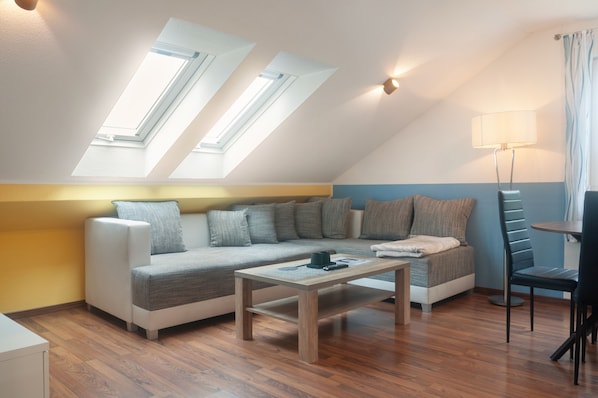 A modern loft-style room with a sloped ceiling, a sofa set, a coffee table, a lamp, and a view through skylights.