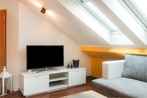 Una sala moderna con un televisor de pantalla plana sobre un mueble blanco, un sofá gris y un tragaluz arriba.